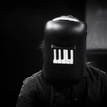 Pohled na muzikanta, v jehož svářečské helmě se odráží klávesy piana